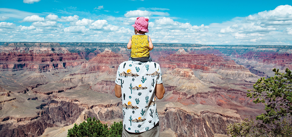 A dad carrying his child on his shoulders as they look out over the Grand Canyon.